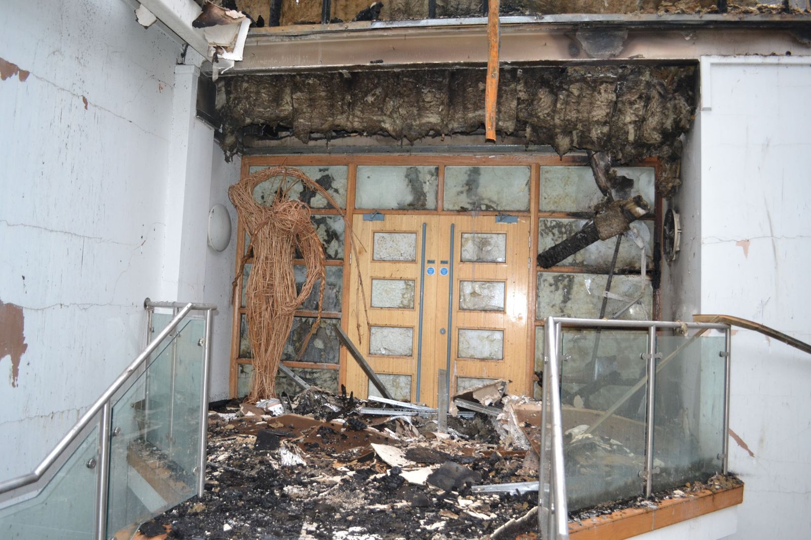 A fire door standing intact in the middle of a burnt-out lobby — the corridor and stairwell behind it are visibly undamaged