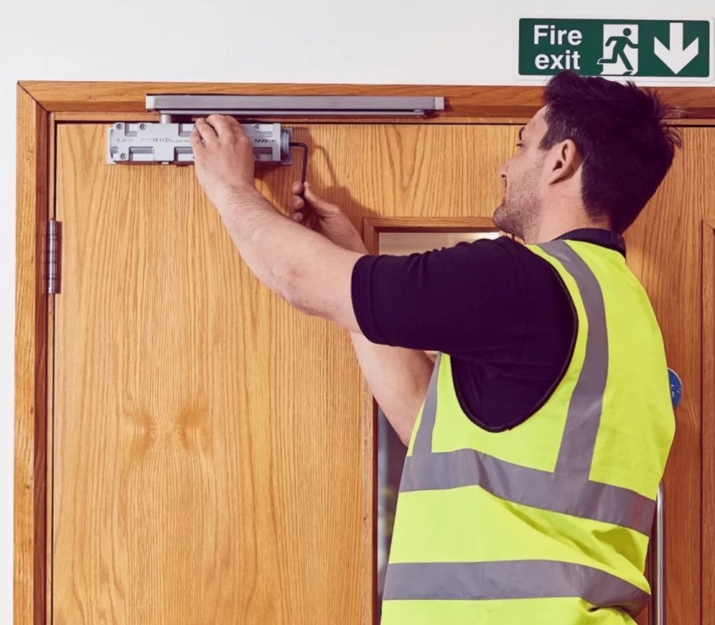 SkyTop fitter installing a fire-door closer beneath a fire exit sign